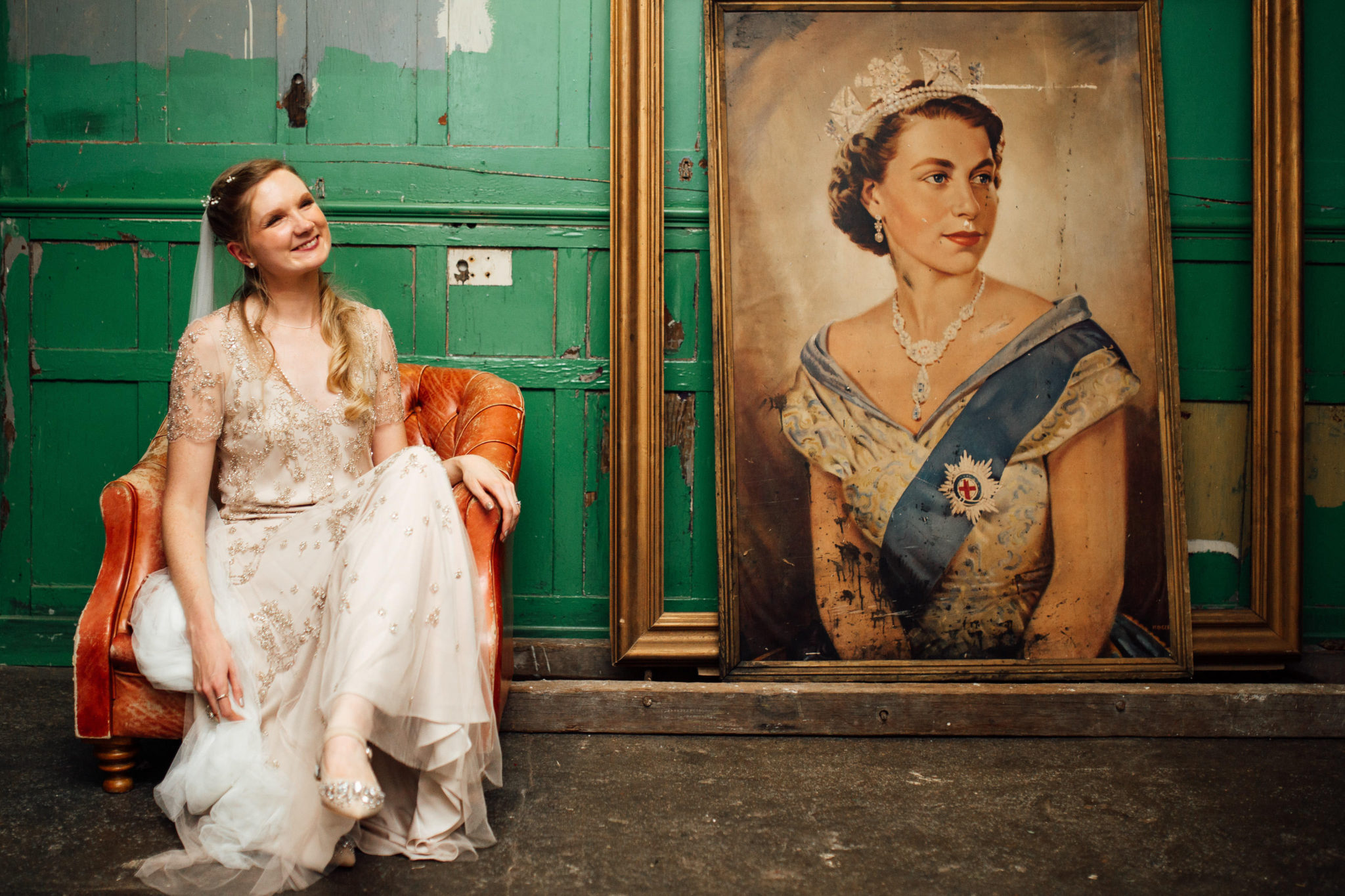 BRIDE POSING NEXT TO QUEEN ELIZABETH PAINTING AT A WEDDING AT ONE FRIENDLY PLACE LONDON DOCUMENTARY FUN WEDDING PHOTOGRAPHY