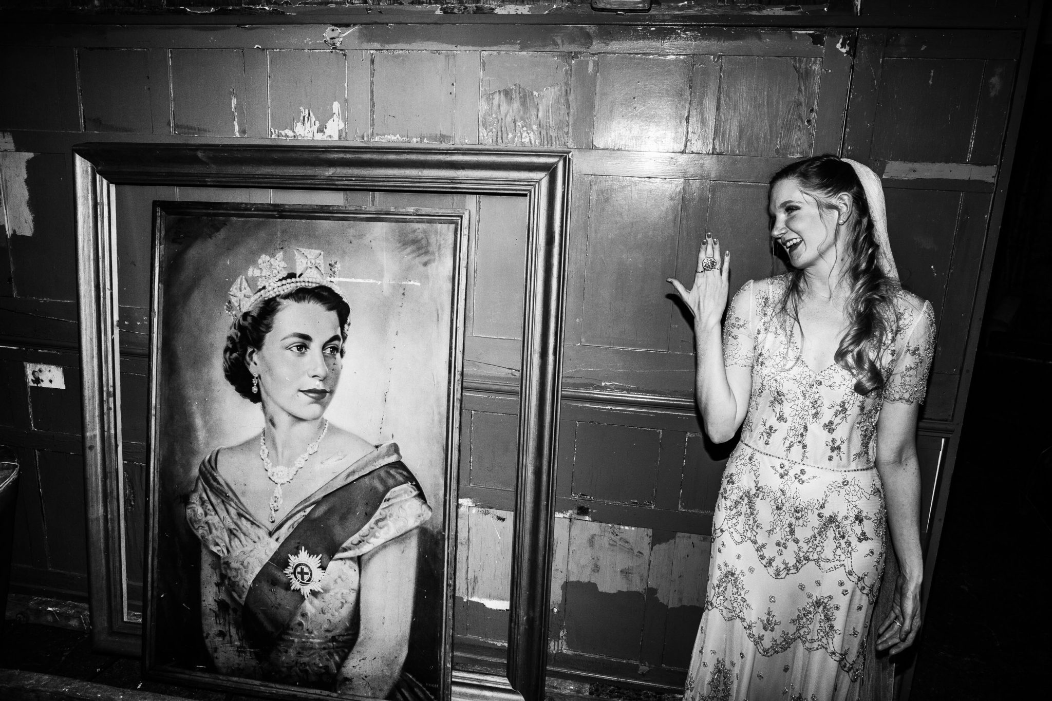 BRIDE POSING NEXT TO QUEEN ELIZABETH PAINTING AT A WEDDING AT ONE FRIENDLY PLACE LONDON DOCUMENTARY FUN WEDDING PHOTOGRAPHY
